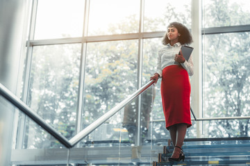 Dazzling African-American businesswoman with a tablet pc is standing on the top of a glass office...