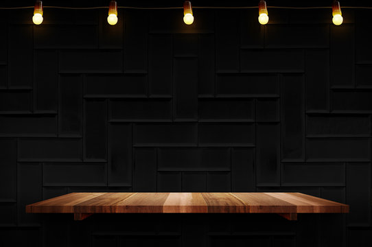 Empty Brown Plank Wood Shelf At Black Modern Tile Wall Background With Light Bulbs String,Mockup For Display Or Montage Of Product Or Design.