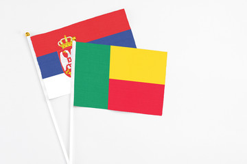 Benin and Serbia stick flags on white background. High quality fabric, miniature national flag. Peaceful global concept.White floor for copy space.