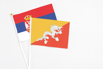 Bhutan and Serbia stick flags on white background. High quality fabric, miniature national flag. Peaceful global concept.White floor for copy space.