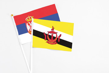 Brunei and Serbia stick flags on white background. High quality fabric, miniature national flag. Peaceful global concept.White floor for copy space.