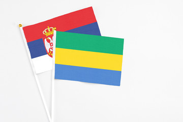 Gabon and Serbia stick flags on white background. High quality fabric, miniature national flag. Peaceful global concept.White floor for copy space.