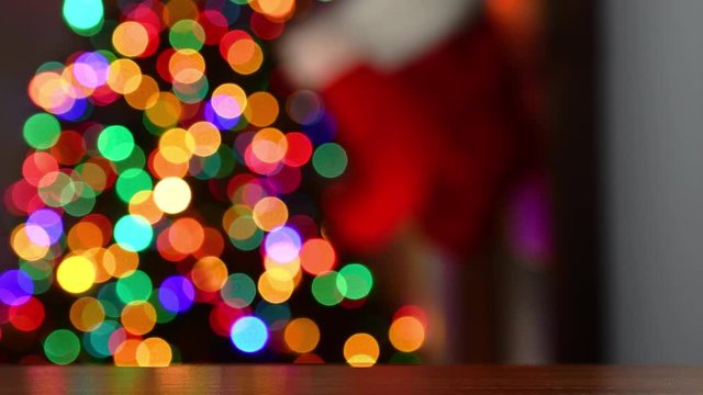 An out of focus Christmas theme background with multi-colored twinkle lights on a Christmas tree as the stocking are hung by the fireplace with a warm glow of a fire at night