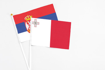 Malta and Serbia stick flags on white background. High quality fabric, miniature national flag. Peaceful global concept.White floor for copy space.