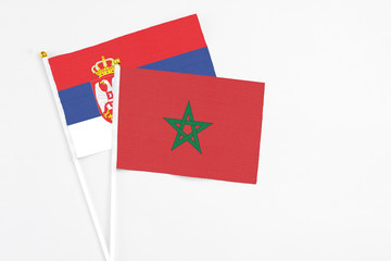 Morocco and Serbia stick flags on white background. High quality fabric, miniature national flag. Peaceful global concept.White floor for copy space.