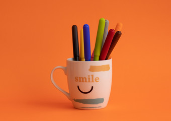 Cup with colorful pencils inside in orange background