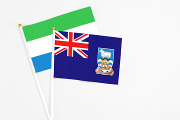 Fototapeta premium Falkland Islands and Sierra Leone stick flags on white background. High quality fabric, miniature national flag. Peaceful global concept.White floor for copy space.