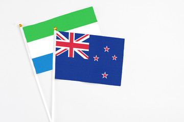 Fototapeta premium New Zealand and Sierra Leone stick flags on white background. High quality fabric, miniature national flag. Peaceful global concept.White floor for copy space.