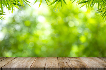 Empty old wooden table top with bamboo leaves frame on blurred greenery background in garden. Copy...