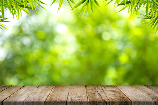 Empty old wooden table top with bamboo leaves frame on blurred greenery background in garden. Copy space for your display or montage product design.