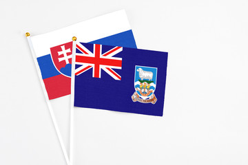 Fototapeta premium Falkland Islands and Slovakia stick flags on white background. High quality fabric, miniature national flag. Peaceful global concept.White floor for copy space.