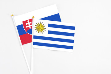 Uruguay and Slovakia stick flags on white background. High quality fabric, miniature national flag. Peaceful global concept.White floor for copy space.