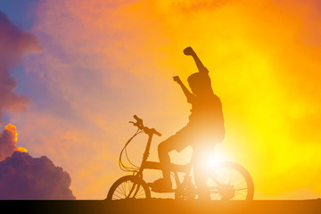 Silhouette of a male sitting on bicycle with a raised hand at sunset