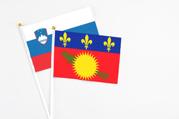 Fototapeta premium Guadeloupe and Slovenia stick flags on white background. High quality fabric, miniature national flag. Peaceful global concept.White floor for copy space.