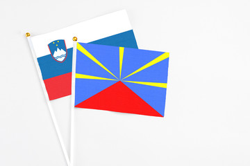 Reunion and Slovenia stick flags on white background. High quality fabric, miniature national flag. Peaceful global concept.White floor for copy space.