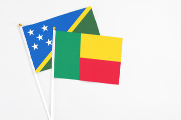 Benin and Solomon Islands stick flags on white background. High quality fabric, miniature national flag. Peaceful global concept.White floor for copy space.