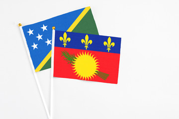 Guadeloupe and Solomon Islands stick flags on white background. High quality fabric, miniature national flag. Peaceful global concept.White floor for copy space.
