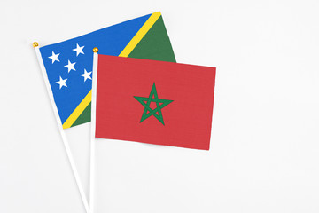 Morocco and Solomon Islands stick flags on white background. High quality fabric, miniature national flag. Peaceful global concept.White floor for copy space.