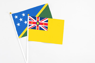 Fototapeta premium Niue and Solomon Islands stick flags on white background. High quality fabric, miniature national flag. Peaceful global concept.White floor for copy space.