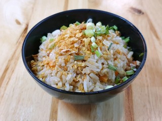Selective focus of fried rice topped with fried garlic in black bowl on wooden table, Ready to eat, on dark background