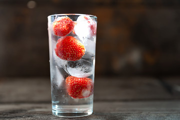 Glass of water with ice and strawberries on a dark background.