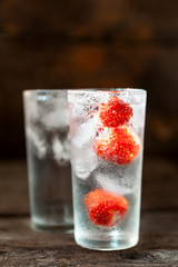 Glass of water with ice and strawberries on a dark background.