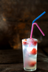 Glass of water with ice and strawberries with cocktail straws on a wooden background.