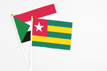 Togo and Sudan stick flags on white background. High quality fabric, miniature national flag. Peaceful global concept.White floor for copy space.