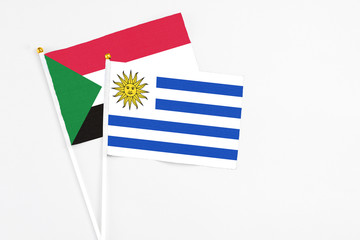 Uruguay and Sudan stick flags on white background. High quality fabric, miniature national flag. Peaceful global concept.White floor for copy space.