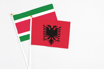Albania and Suriname stick flags on white background. High quality fabric, miniature national flag. Peaceful global concept.White floor for copy space.