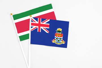 Fototapeta premium Cayman Islands and Suriname stick flags on white background. High quality fabric, miniature national flag. Peaceful global concept.White floor for copy space.