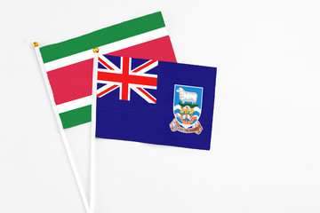 Fototapeta premium Falkland Islands and Suriname stick flags on white background. High quality fabric, miniature national flag. Peaceful global concept.White floor for copy space.