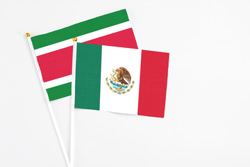 Mexico and Suriname stick flags on white background. High quality fabric, miniature national flag. Peaceful global concept.White floor for copy space.
