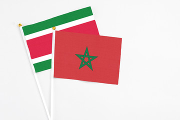 Morocco and Suriname stick flags on white background. High quality fabric, miniature national flag. Peaceful global concept.White floor for copy space.