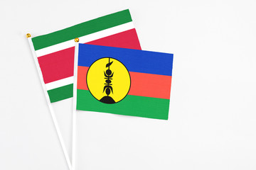 New Caledonia and Suriname stick flags on white background. High quality fabric, miniature national flag. Peaceful global concept.White floor for copy space.