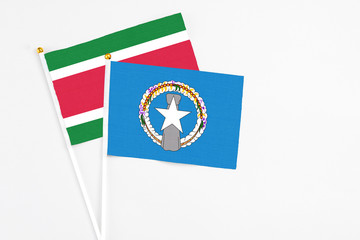 Northern Mariana Islands and Suriname stick flags on white background. High quality fabric, miniature national flag. Peaceful global concept.White floor for copy space.