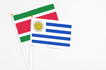 Uruguay and Suriname stick flags on white background. High quality fabric, miniature national flag. Peaceful global concept.White floor for copy space.