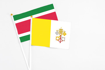 Vatican City and Suriname stick flags on white background. High quality fabric, miniature national flag. Peaceful global concept.White floor for copy space.