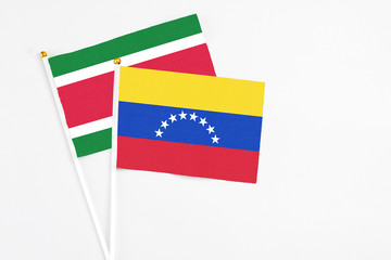 Venezuela and Suriname stick flags on white background. High quality fabric, miniature national flag. Peaceful global concept.White floor for copy space.