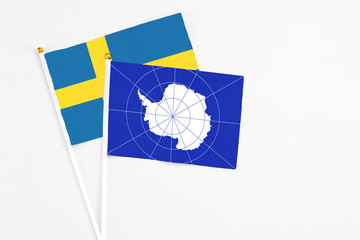 Antarctica and Sweden stick flags on white background. High quality fabric, miniature national flag. Peaceful global concept.White floor for copy space.