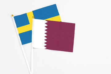 Qatar and Sweden stick flags on white background. High quality fabric, miniature national flag. Peaceful global concept.White floor for copy space.