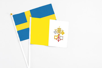 Vatican City and Sweden stick flags on white background. High quality fabric, miniature national flag. Peaceful global concept.White floor for copy space.