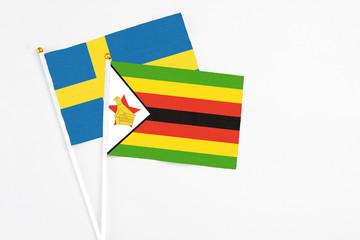 Zimbabwe and Sweden stick flags on white background. High quality fabric, miniature national flag. Peaceful global concept.White floor for copy space.