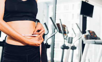 Beautiful woman using tape measuring waist, her is body slim after workout at fitness GYM