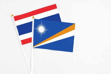 Fototapeta premium Marshall Islands and Thailand stick flags on white background. High quality fabric, miniature national flag. Peaceful global concept.White floor for copy space.