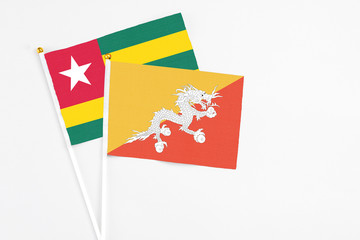 Bhutan and Togo stick flags on white background. High quality fabric, miniature national flag. Peaceful global concept.White floor for copy space.