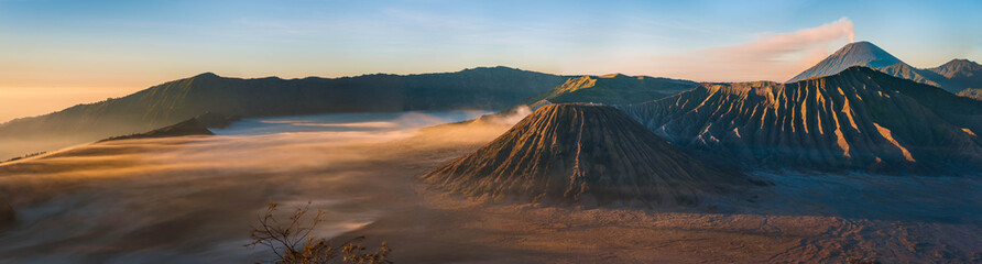 Sunrise panorama of Mount Bromo, in the Tengger Caldera, with Semeru volcano behind. Glowing orange mist recedes from the Tengger Sand Sea, Indonesia's only desert landscape; Pananjakan, Java