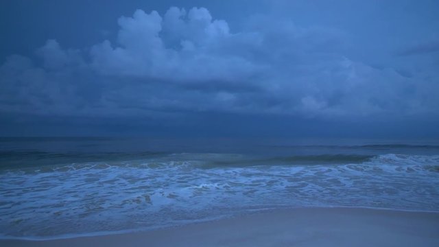 Lightning strikes and flashes in the sky as dark and stormy sea waves usher in the rain clouds at dusk on the beaches of Southern Alabama near the tourist coastal town of Gulf Shores, USA.