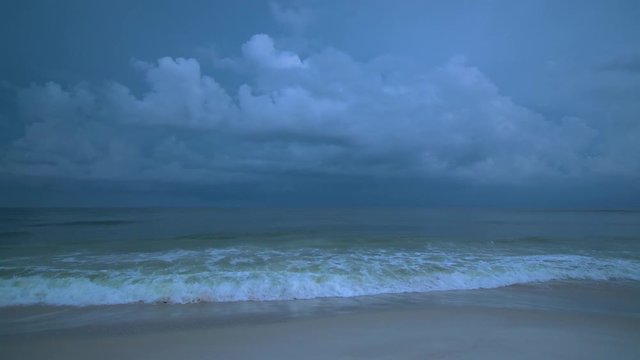 Brilliant glowing purple lightning strikes, flashes and illuminates the stormy sky above the ocean as waves crash the white sandy beaches of Florida as a hurricane approaches in dangerous weather. 