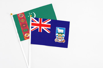 Fototapeta premium Falkland Islands and Turkmenistan stick flags on white background. High quality fabric, miniature national flag. Peaceful global concept.White floor for copy space.
